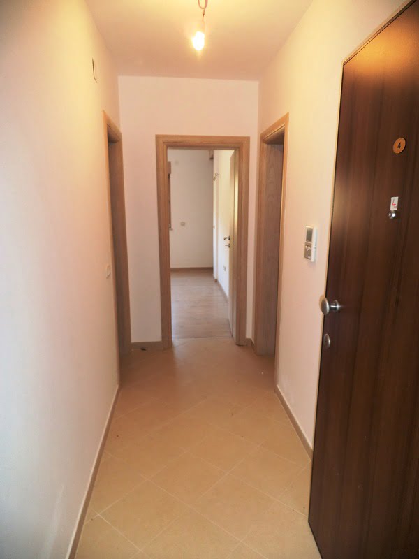 Bright hallway in an apartment in Bečići, Montenegro: tiled floor, light wood interior doors, and an entrance door.