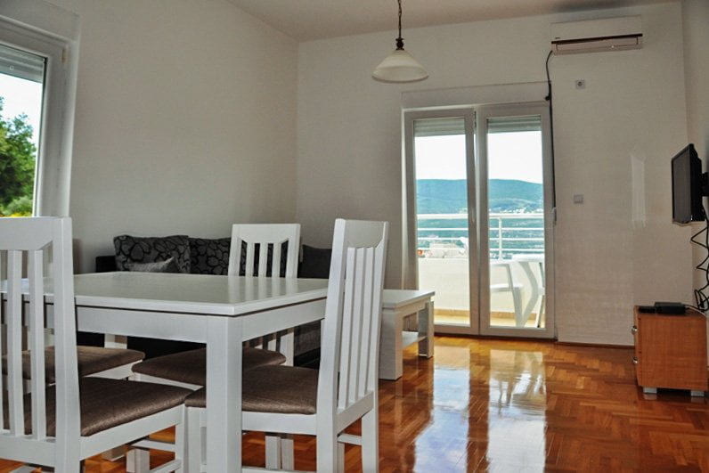 Living room with white furniture, parquet flooring, and access to a terrace with mountain views in an apartment, Herceg Novi, Montenegro.