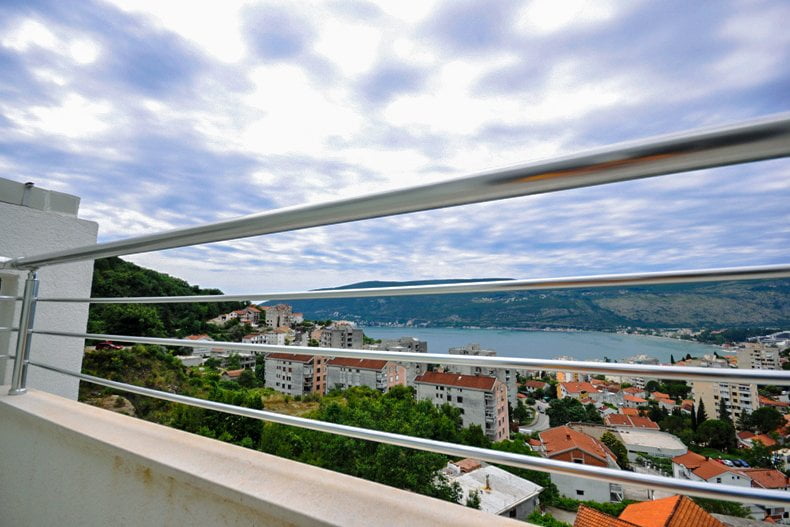 View from the apartment balcony in Herceg Novi, Montenegro: a panorama of the city, mountains, and the Adriatic Sea with a metal railing.