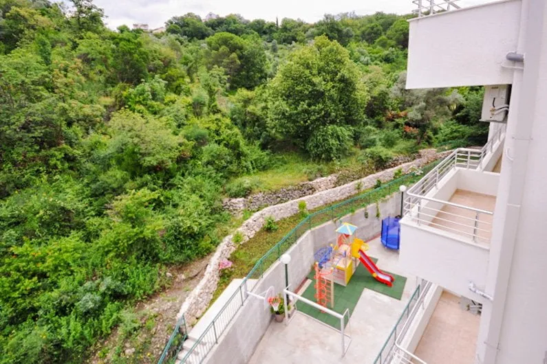 Outdoor playground with a slide and trampoline next to a building, surrounded by dense green forest.