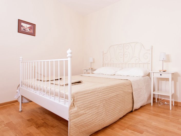 Bright bedroom with a white wrought-iron bed in an apartment for sale in Herceg Novi, Montenegro: parquet flooring and a cozy interior.