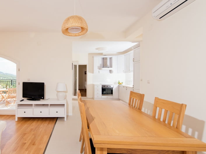 Bright living room with dining area and kitchen in an apartment, Herceg Novi, Montenegro: wooden table, TV, and access to the terrace.