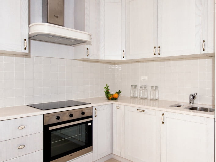 Bright kitchen in an apartment in Herceg Novi, Montenegro: white cabinet fronts, built-in appliances, a stove, and a tiled backsplash.