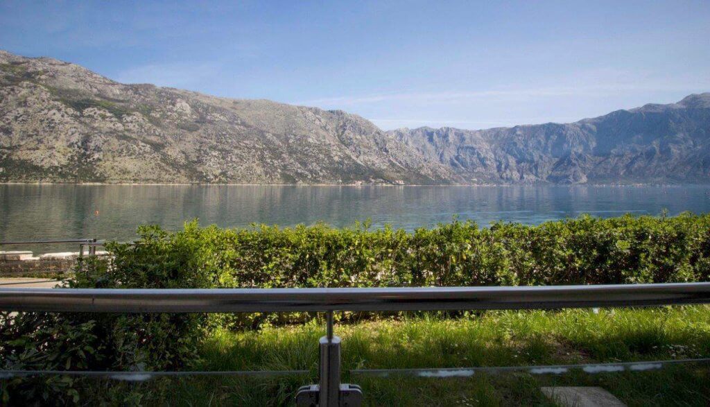 View from the apartment balcony in Stoliv, Bay of Kotor, Montenegro: a panorama of the sea and mountains through greenery.