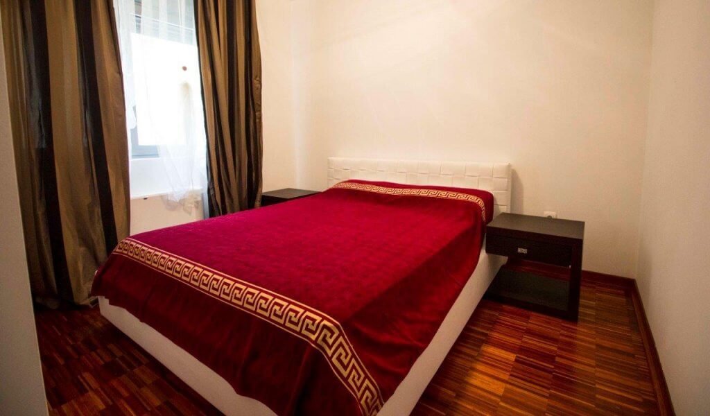 Cozy bedroom with a double bed in an apartment in Stoliv, Bay of Kotor, Montenegro. Parquet flooring and dark curtains.