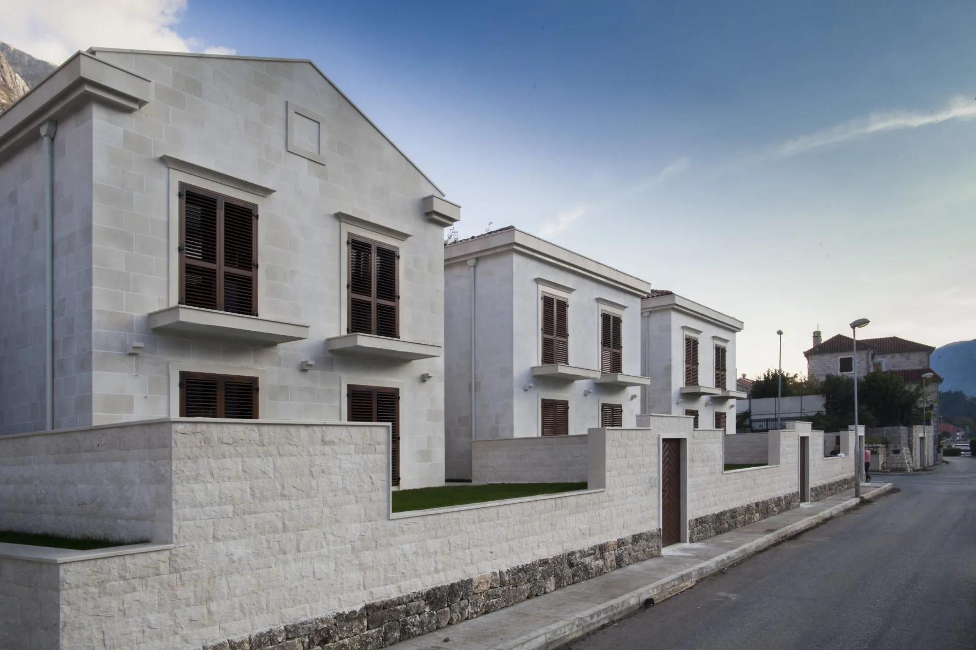 Exterior view of modern stone houses with wooden shutters and a street-facing wall.