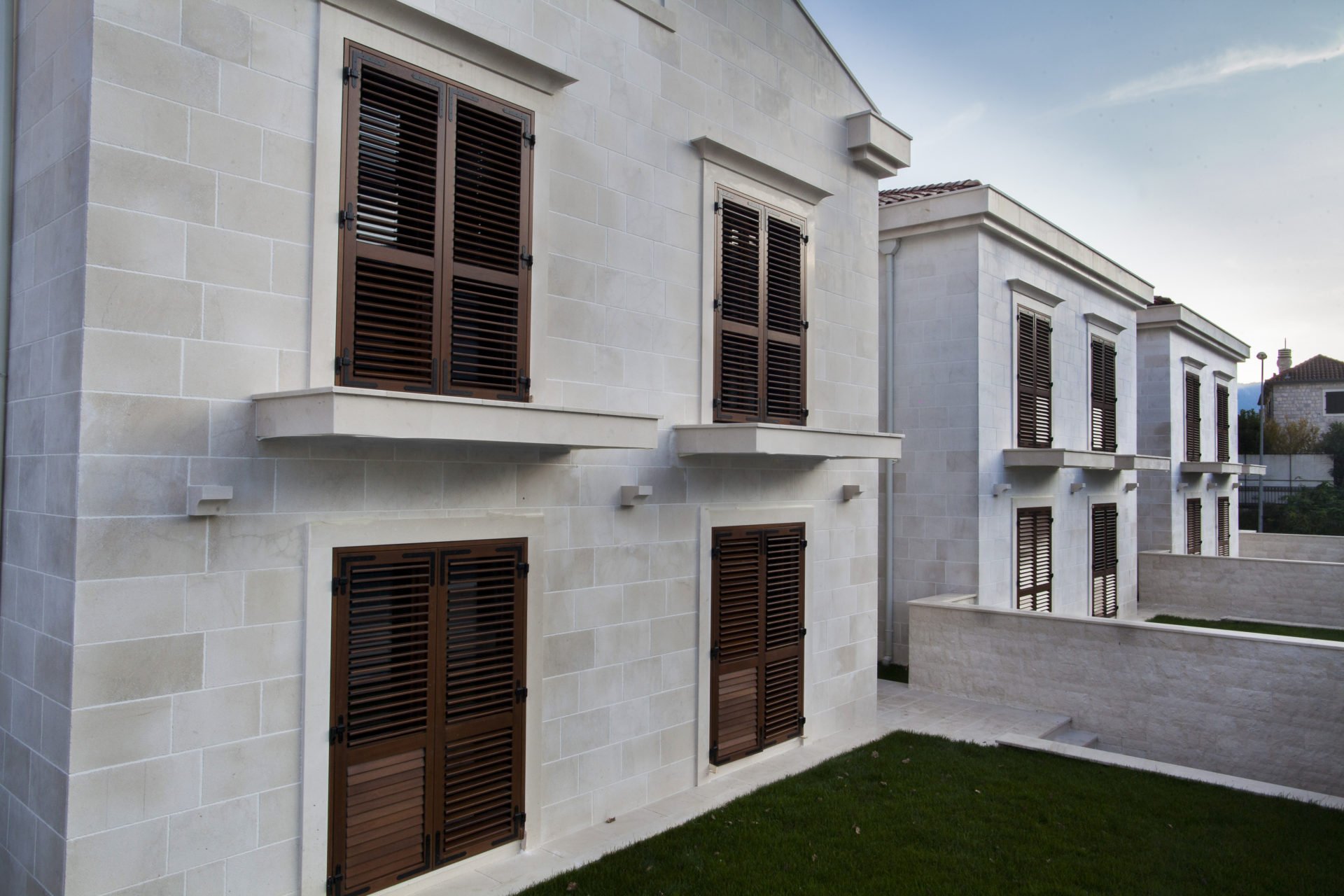 Facade of a residential complex in Dobrota, Montenegro: stone wall cladding and brown wooden shutters on the windows.