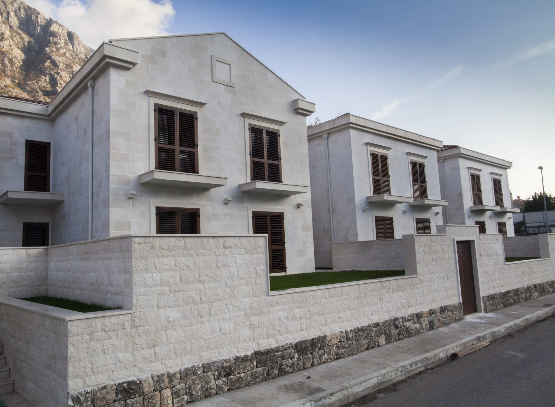 Modern villas made of light stone with brown shutters in a residential complex, Dobrota, Montenegro.