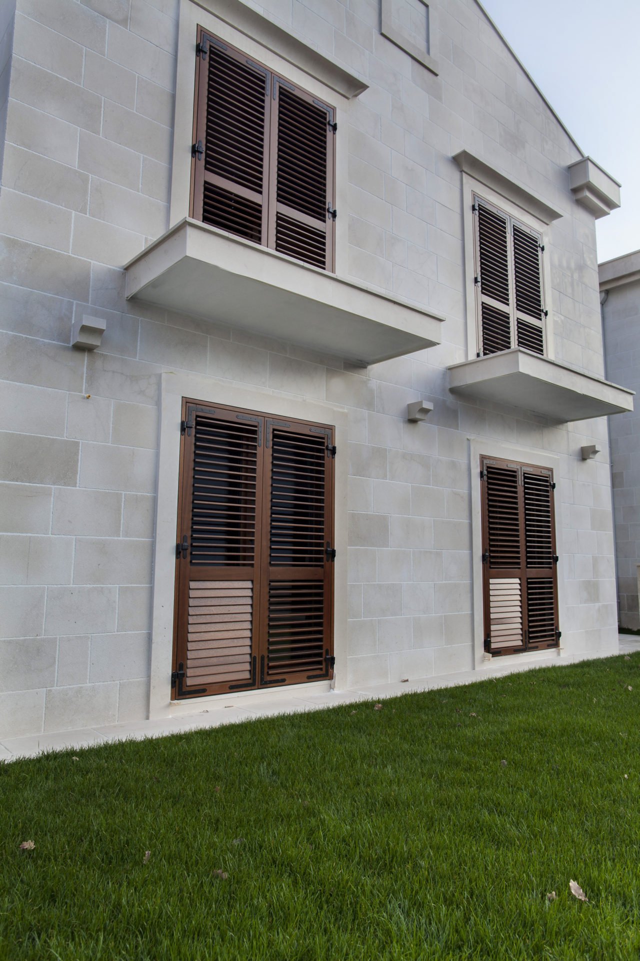 Facade of a residential complex in Dobrota, Montenegro: stone wall cladding, brown wooden shutters, and a green lawn.