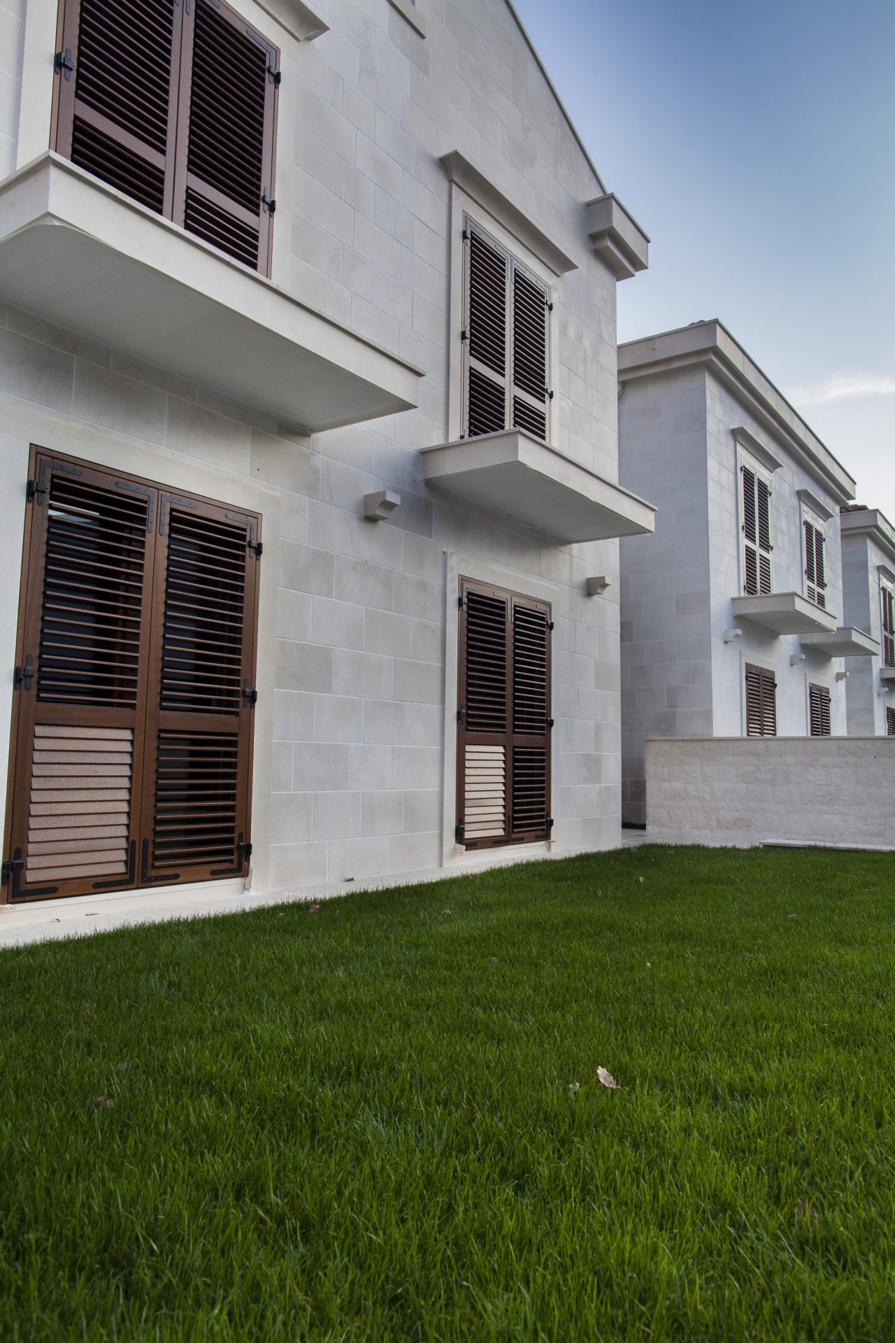 Facade of a modern residential complex in Dobrota, Montenegro: stone cladding, brown shutters, and a well-kept lawn.