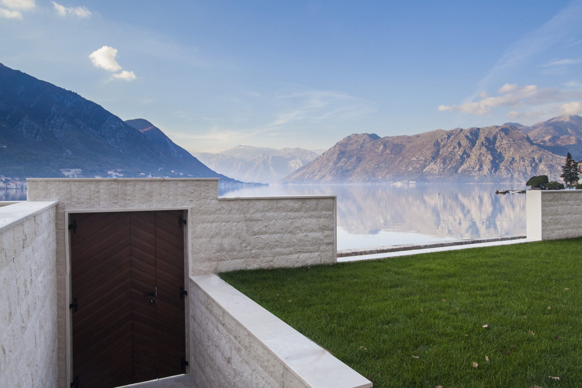 View of the Bay of Kotor and the mountains from the terrace of the complex in Dobrota, Montenegro: stone finish and green lawn.