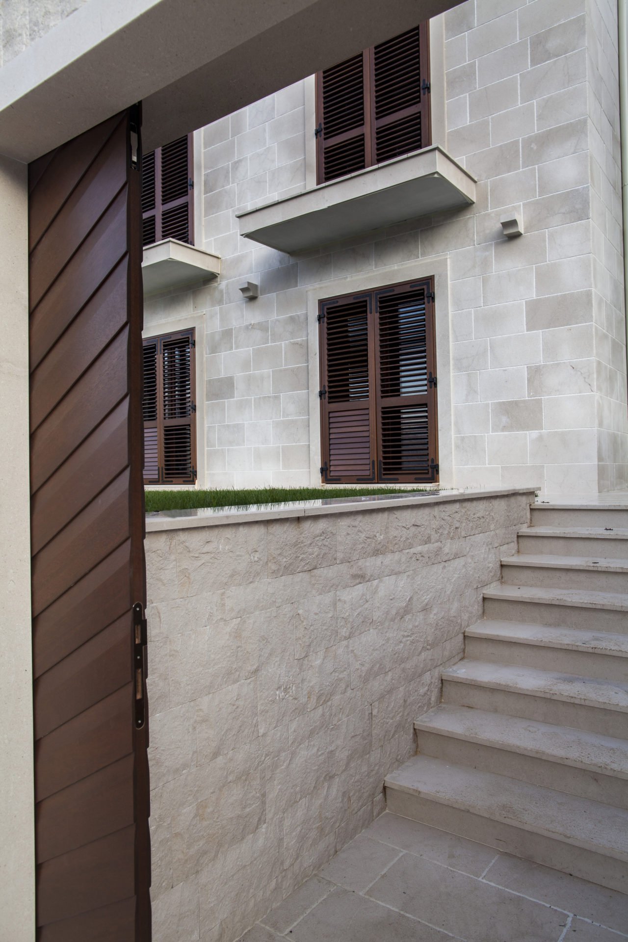 Facade of a residential complex in Dobrota, Montenegro: stone cladding, wooden shutters, and a staircase leading to the grounds.