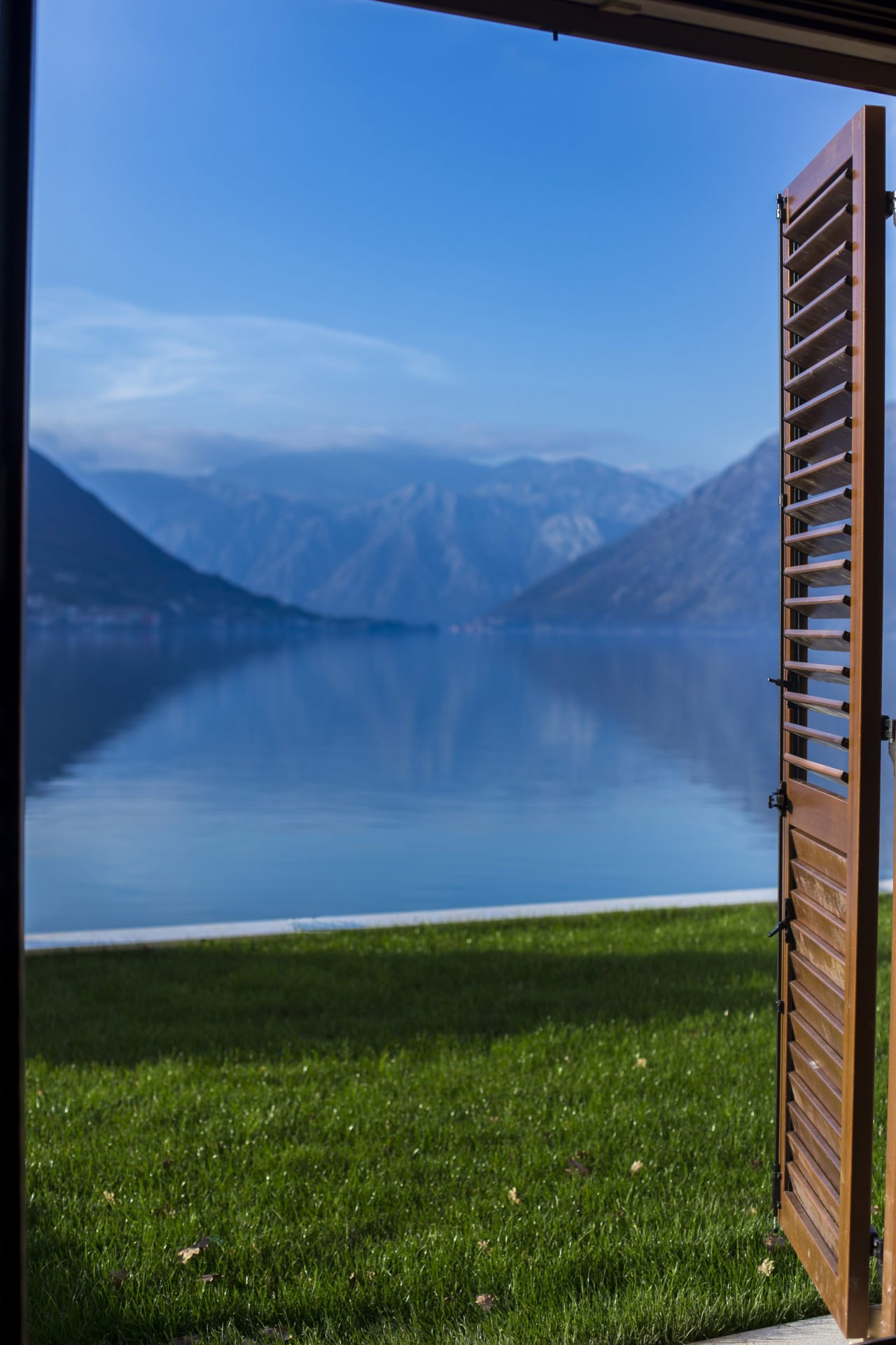 View of the Bay of Kotor and the mountains from the bedroom of a residential complex in Dobrota, Montenegro, with open wooden shutters.