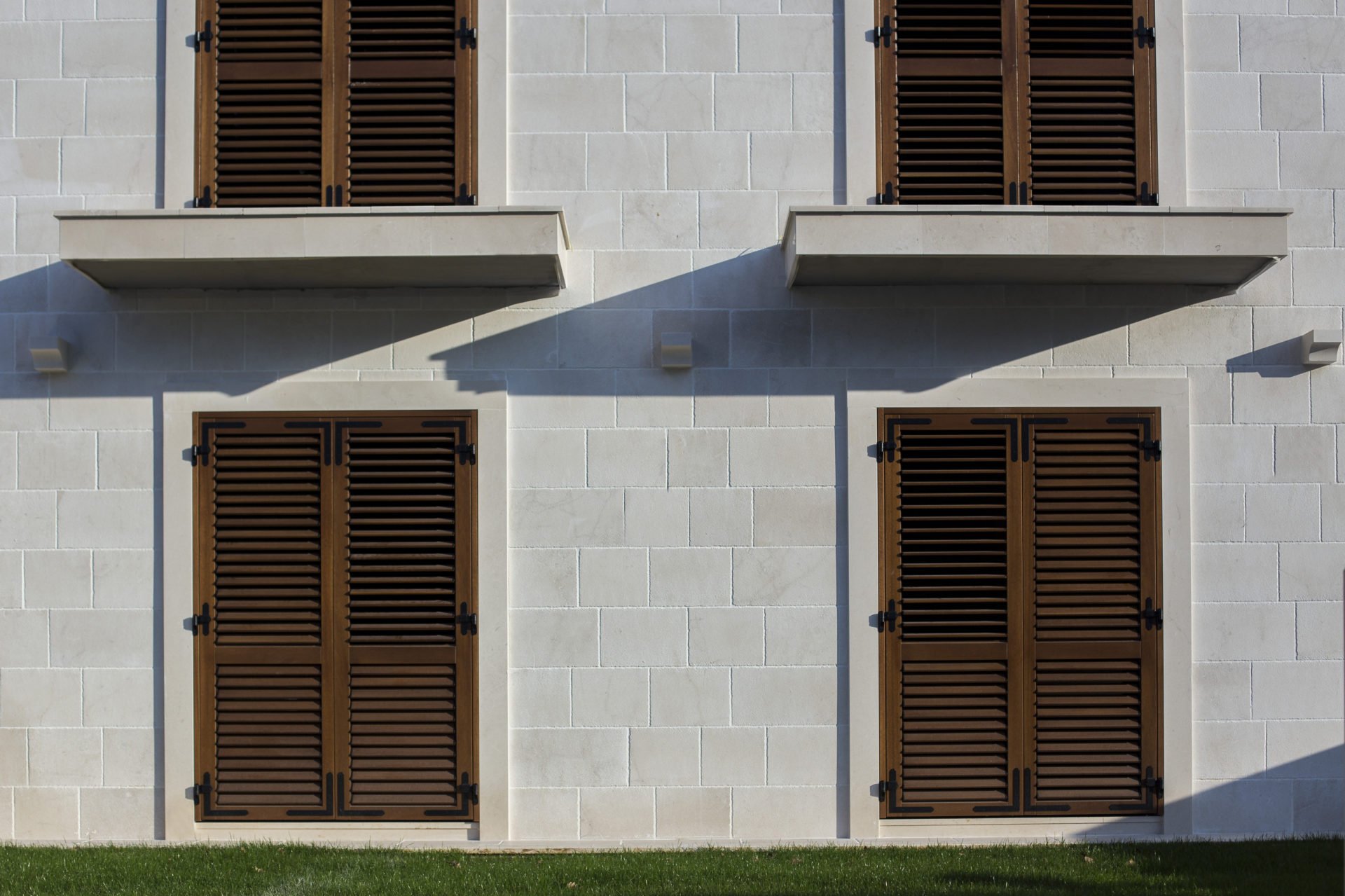 Facade of a residential complex in Dobrota, Montenegro: white stone masonry and brown wooden shutters on the windows.