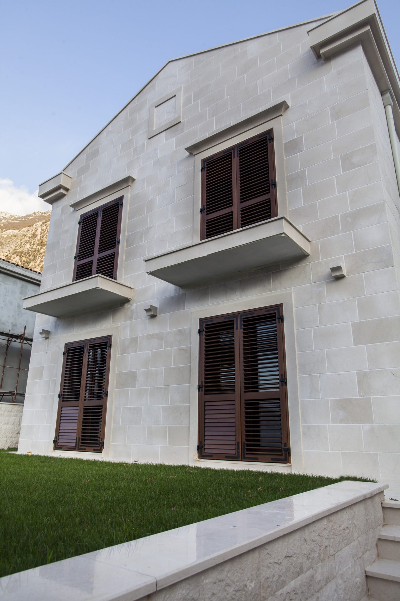 Facade of a modern house made of light stone with brown shutters in Dobrota, Montenegro.
