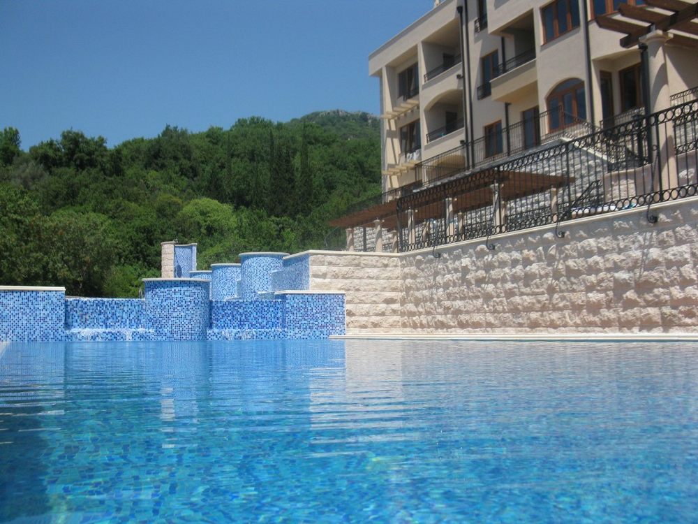 Outdoor pool with a cascade at a residential complex in Igalo, Herceg Novi, Montenegro, against a backdrop of mountains and greenery.