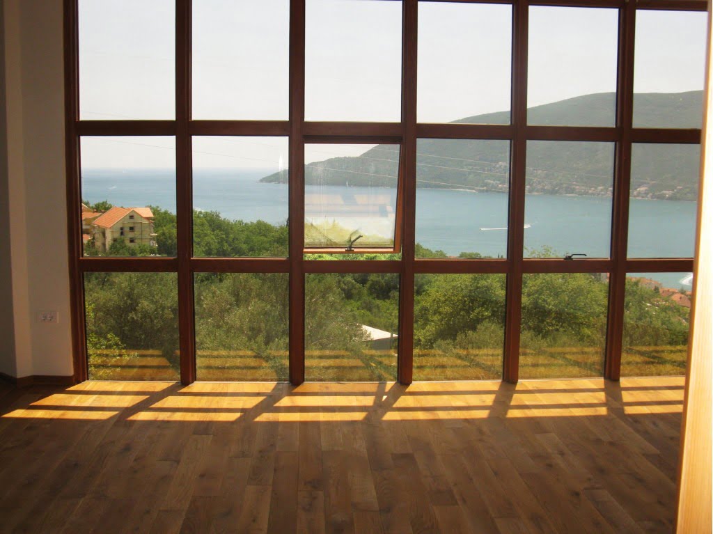 Panoramic window in the living room with a view of the sea and mountains, Igalo, Montenegro. Bright room with wooden flooring.
