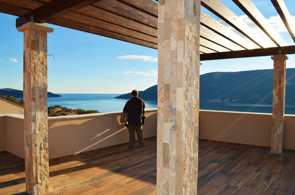 Spacious terrace with sea view in a residential complex in Igalo, Montenegro: stone columns and wooden decking.