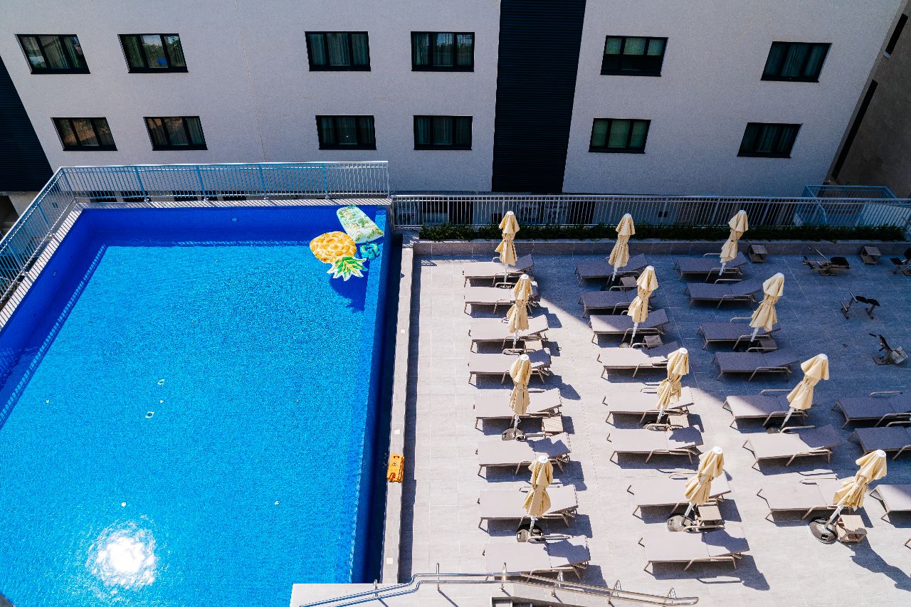 Outdoor swimming pool with sun loungers and umbrellas at a beachfront residential complex in Rafailovici, Montenegro.