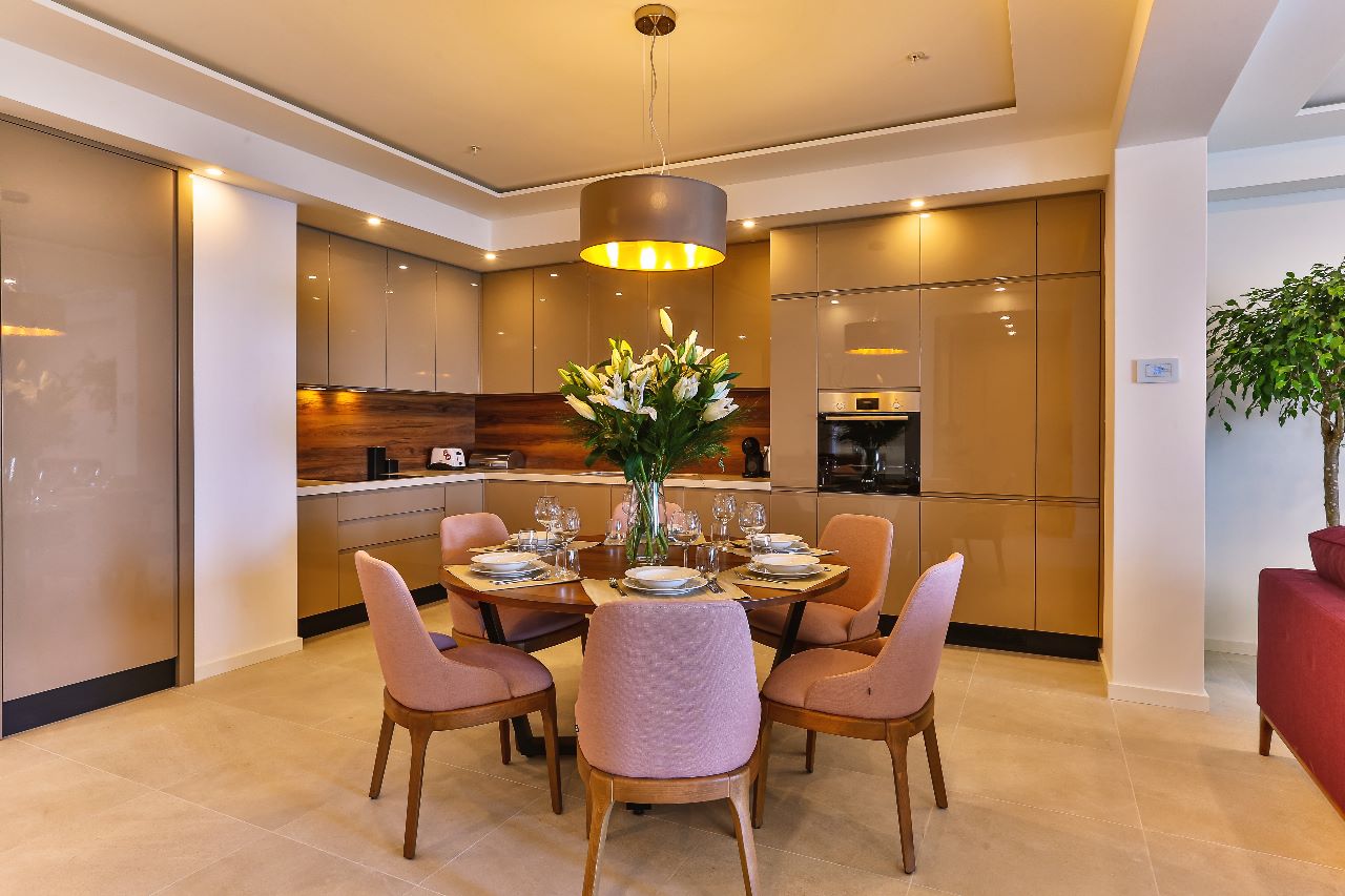 Modern kitchen-dining room in a residential complex in Rafailovici, Montenegro: glossy cabinets, dining area with pink chairs.
