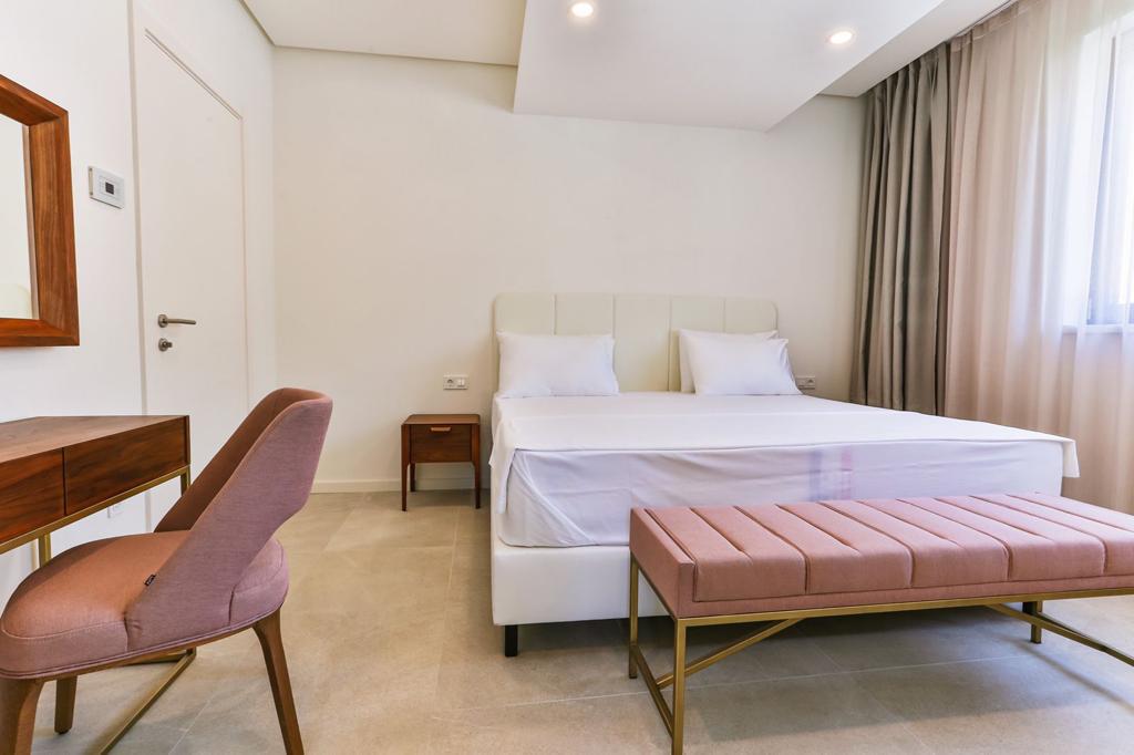 Bright bedroom with a double bed and a pink bench in a beachfront residential complex, Rafailovici, Montenegro.