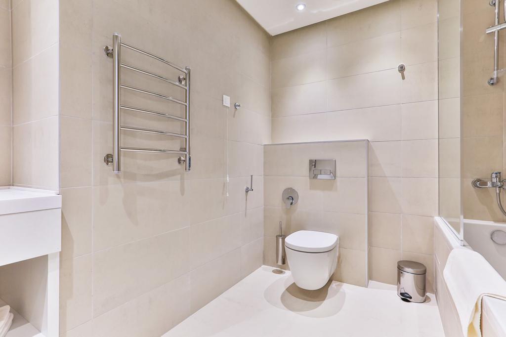 Modern bathroom with beige tiles, wall-hung toilet, and heated towel rail in the Rafailovici residential complex, Montenegro.