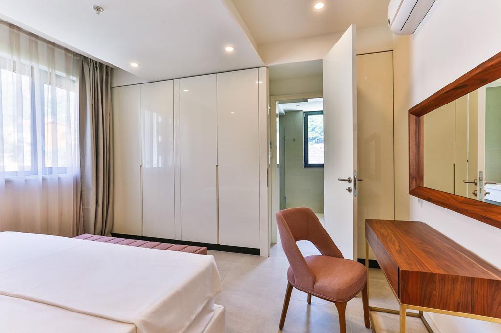 Modern bedroom in Rafailovici residential complex, Montenegro: white wardrobe, vanity table with a mirror, and mountain view.