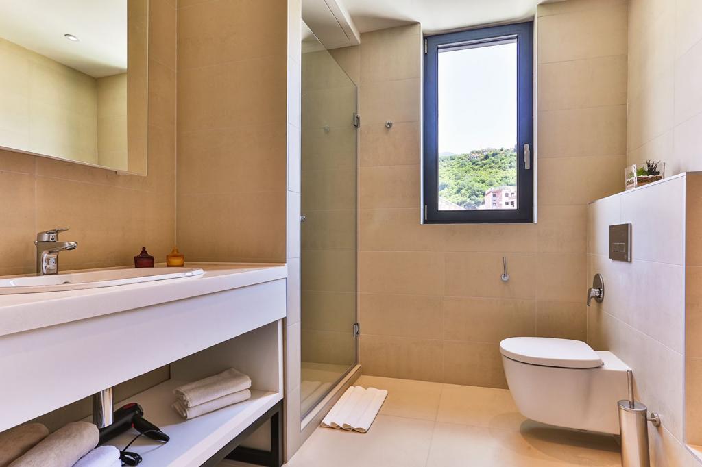 Modern bathroom with a walk-in shower in a residential complex in Rafailovici, Montenegro: light-colored tiles and a view from the window.