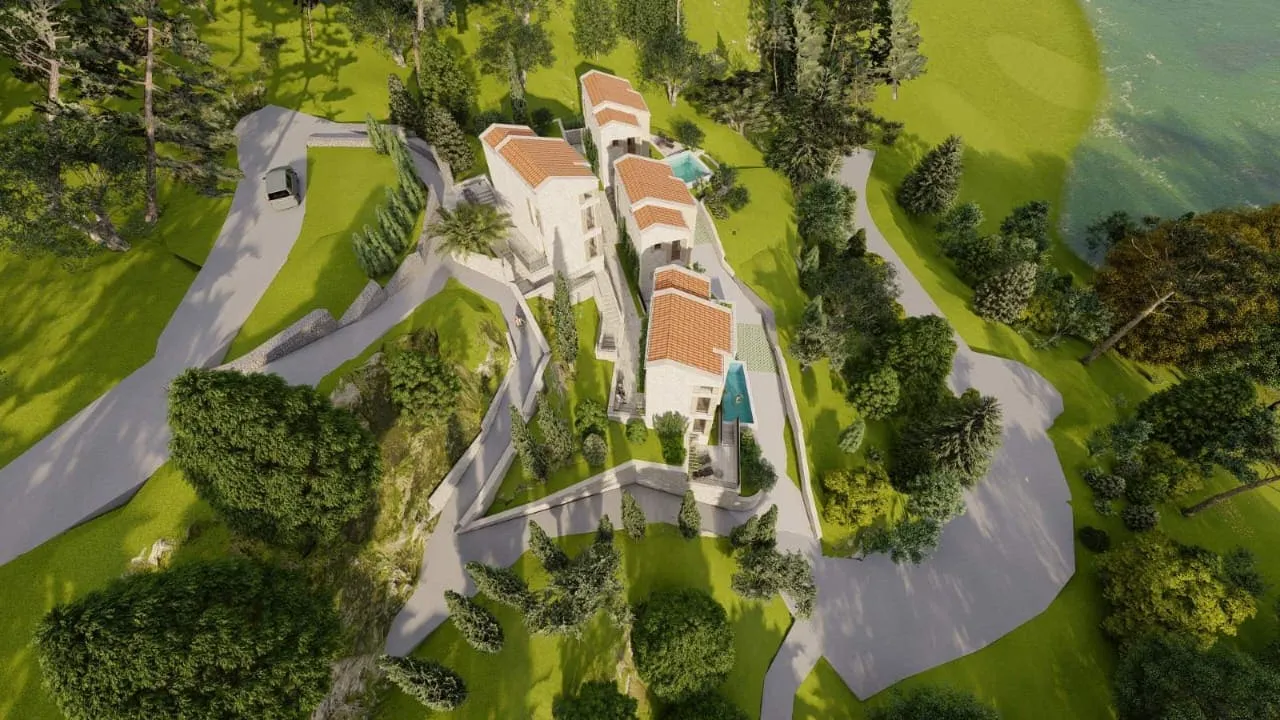 Aerial view of a villa with terracotta roofs, pools, and winding paths on a green hillside near water.