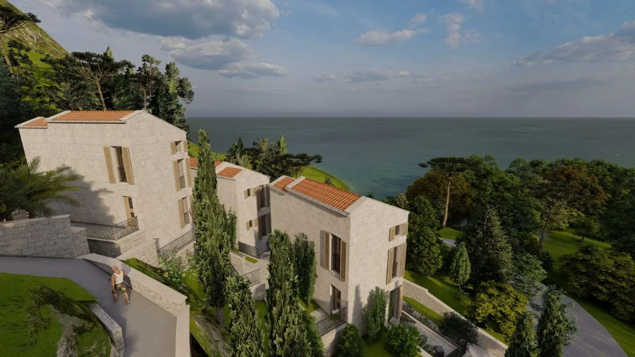 Stone houses with terracotta roofs on a seaside hillside surrounded by trees and greenery.