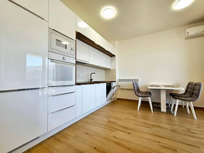Modern white kitchen with appliances and dining area in an apartment in Budva, Montenegro. Bright interior with laminate flooring.