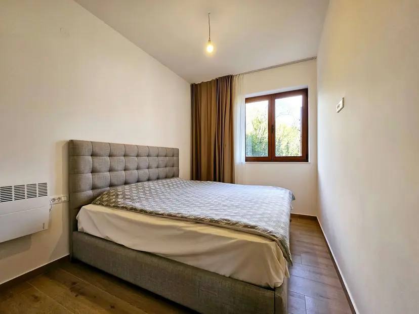 Cozy bedroom with a double bed in an apartment in Budva, Montenegro: bright interior, parquet flooring, and a view from the window.