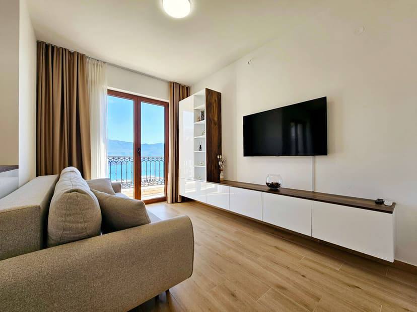 Living room in a modern apartment in Budva, Montenegro: sofa, TV area, and a balcony with panoramic sea views.