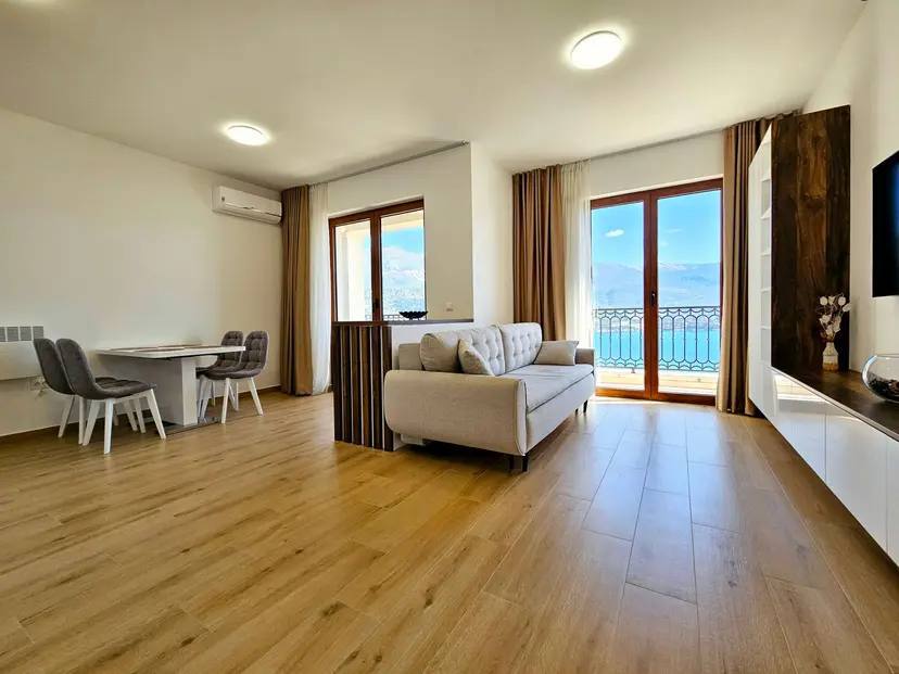 Modern living room in an apartment in Budva, Montenegro: light-colored furniture, dining area, and panoramic sea view.
