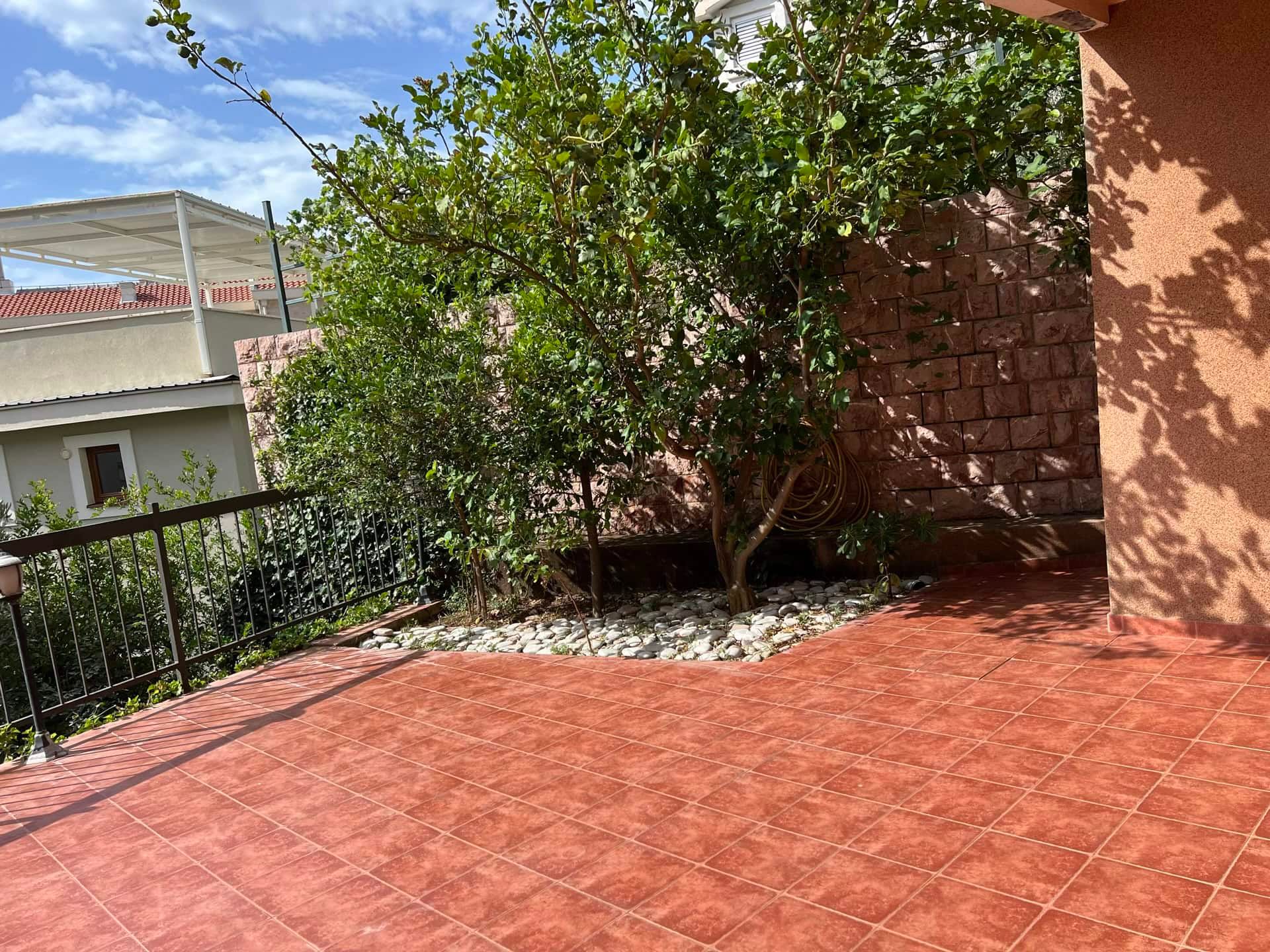 Cozy terrace with tile and a green tree in a duplex, Petrovac, Montenegro. View of a private courtyard with a stone wall.