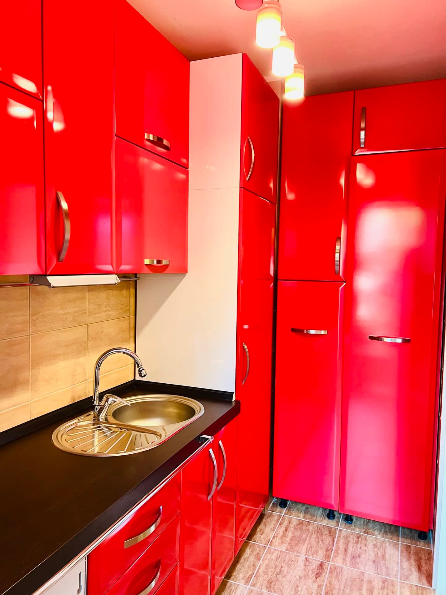 Bright kitchen with red glossy cabinets in an apartment, Petrovac, Montenegro: black countertop and built-in appliances.