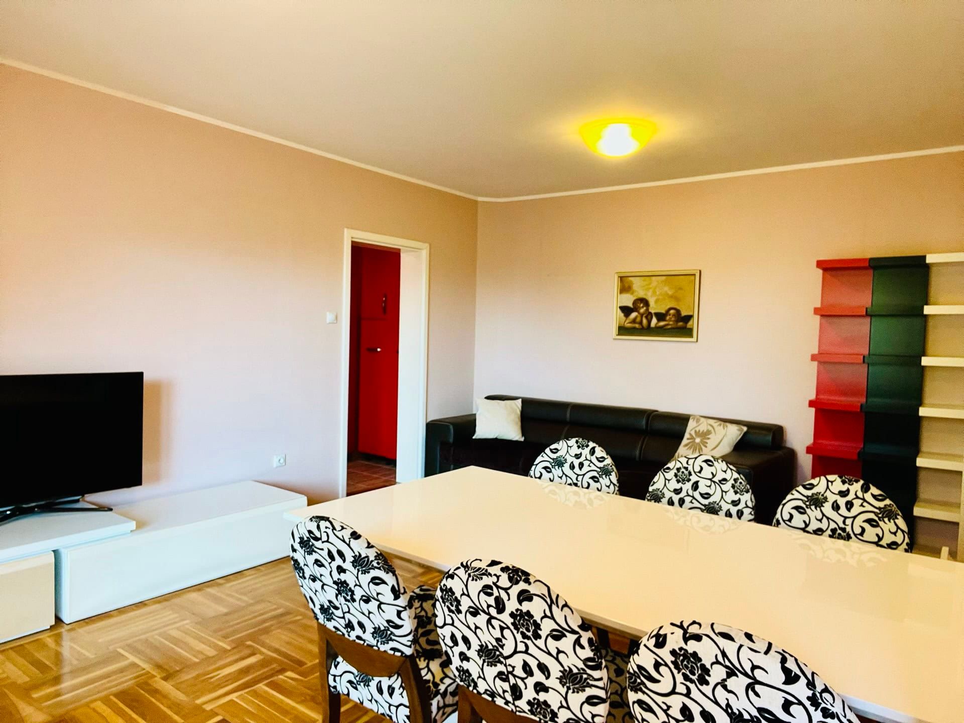 Living room in a duplex in Petrovac, Montenegro: dining area with a white table, floral-print chairs, and a TV area.