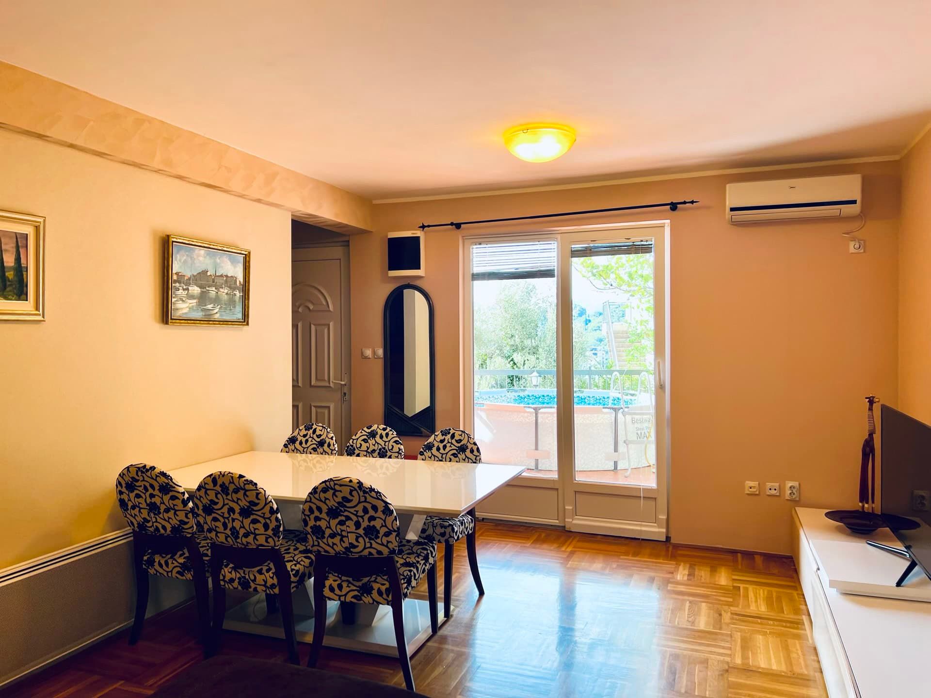 Living room with dining area in an apartment in Petrovac, Montenegro: parquet flooring, access to a terrace with a pool, and air conditioning.