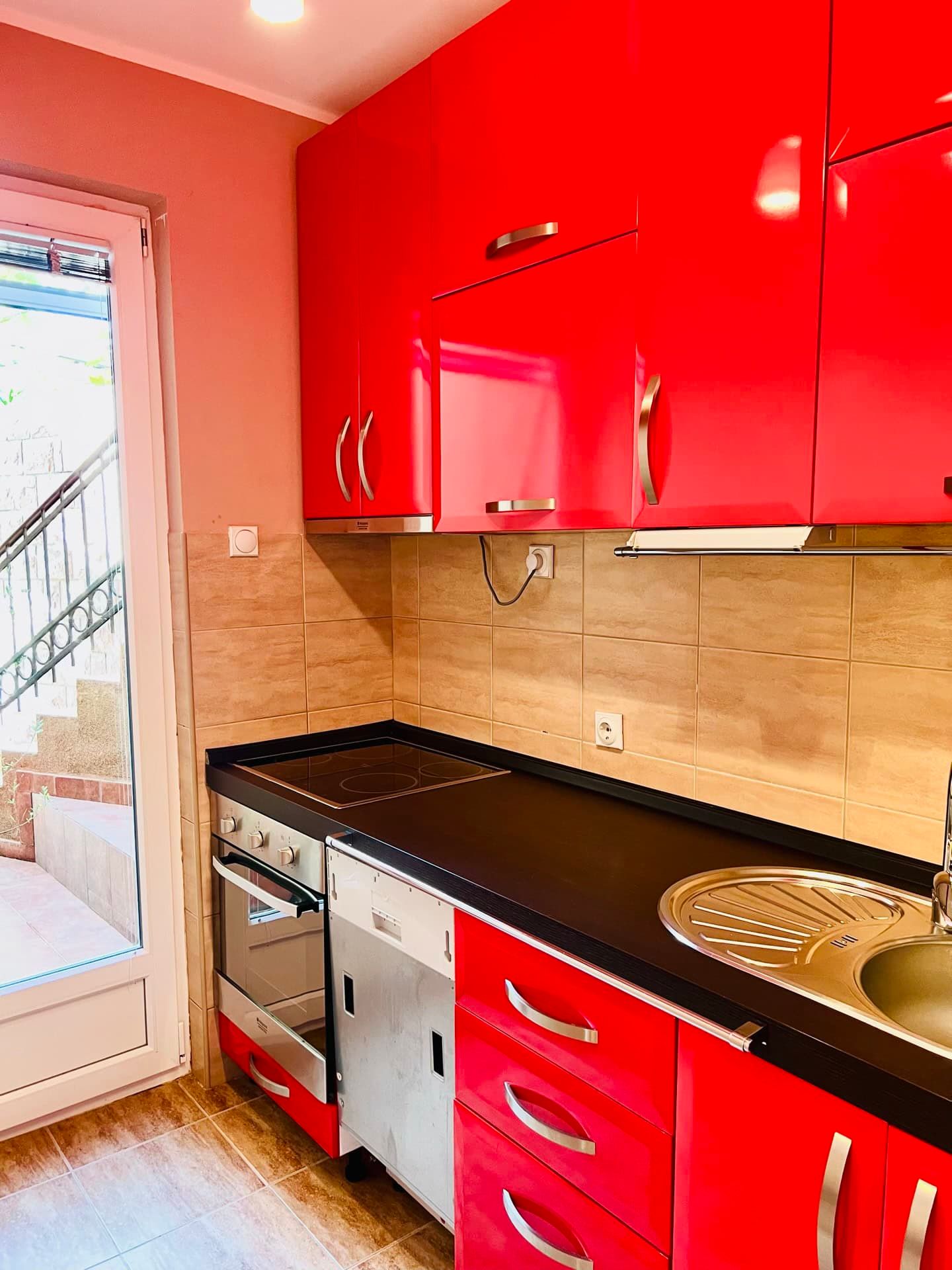 Bright kitchen with red glossy cabinets in an apartment in Petrovac, Montenegro, with access to the terrace and built-in appliances