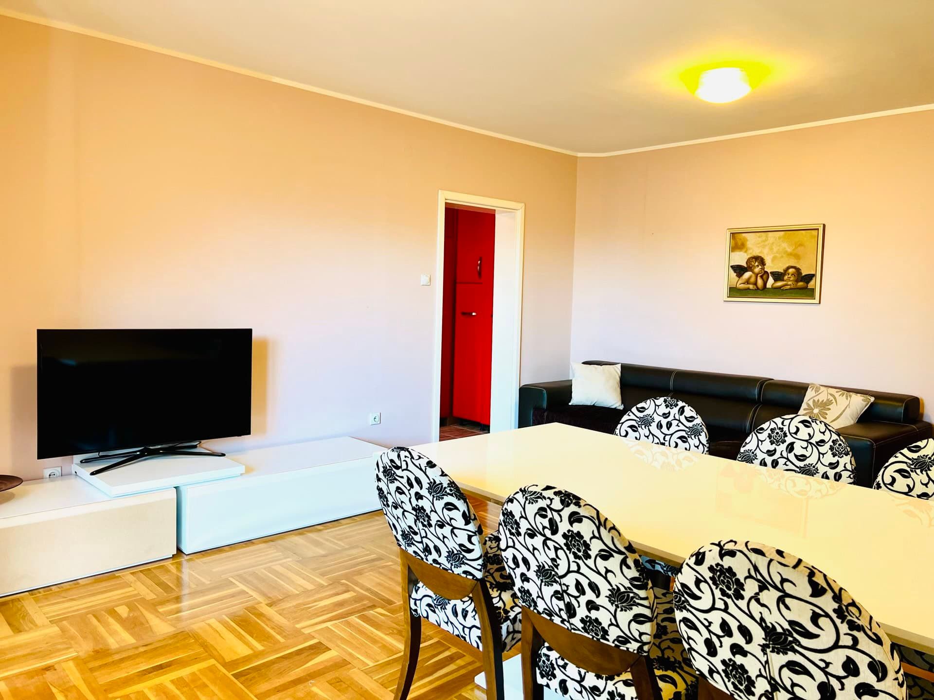 Living room in a duplex in Petrovac, Montenegro: dining area with patterned chairs, TV area, and a black leather sofa.