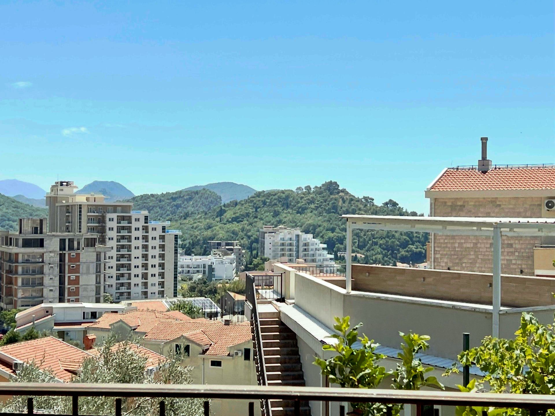 View from the balcony of a duplex in Petrovac, Montenegro: a city panorama, tiled roofs, and green mountains on the horizon.
