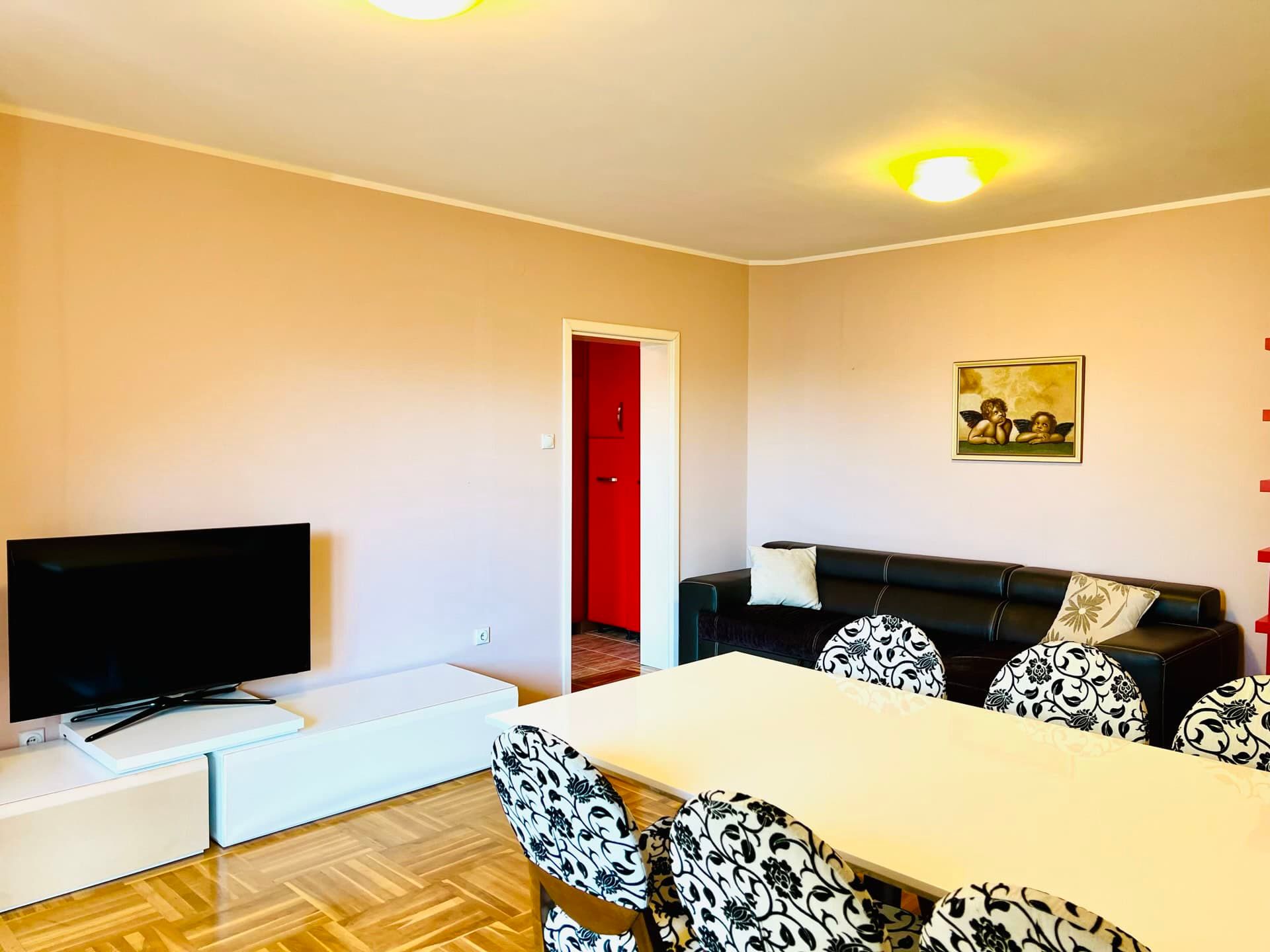 Living room in a duplex in Petrovac, Montenegro: black sofa, dining table with chairs, and TV area with parquet flooring.
