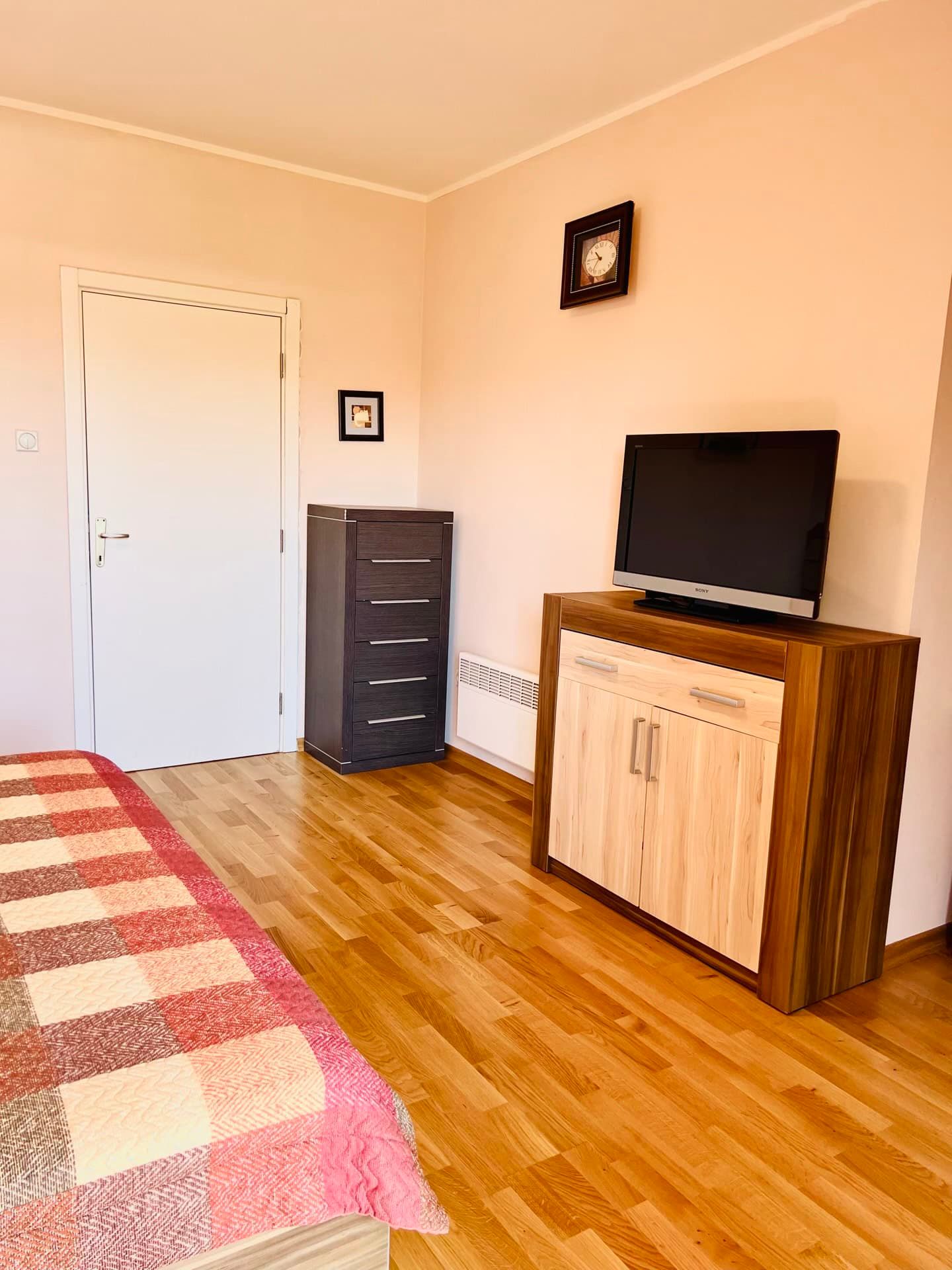 Bedroom in an apartment in Petrovac, Montenegro: parquet floor, dresser, TV stand, and a bed with a checkered bedspread.