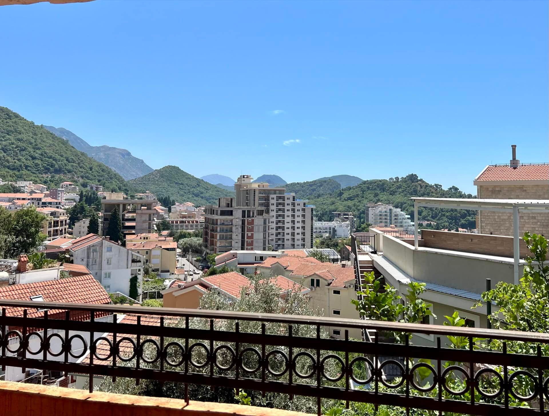 View from the balcony of a duplex in Petrovac, Montenegro: city panorama, tiled roofs, and green mountains on the horizon.