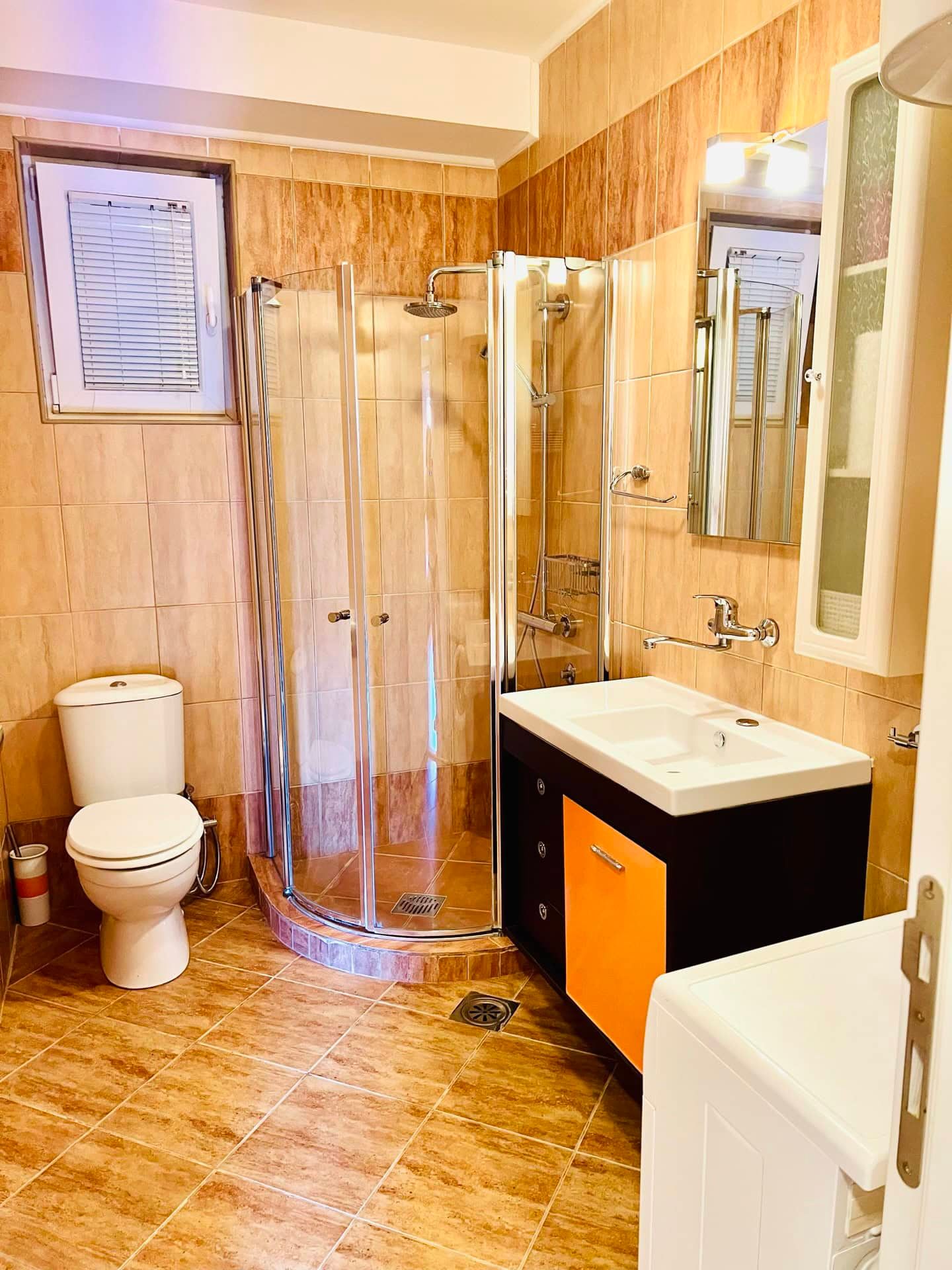 Bathroom in an apartment in Petrovac, Montenegro: shower cabin, vanity with sink, and beige tile interior.