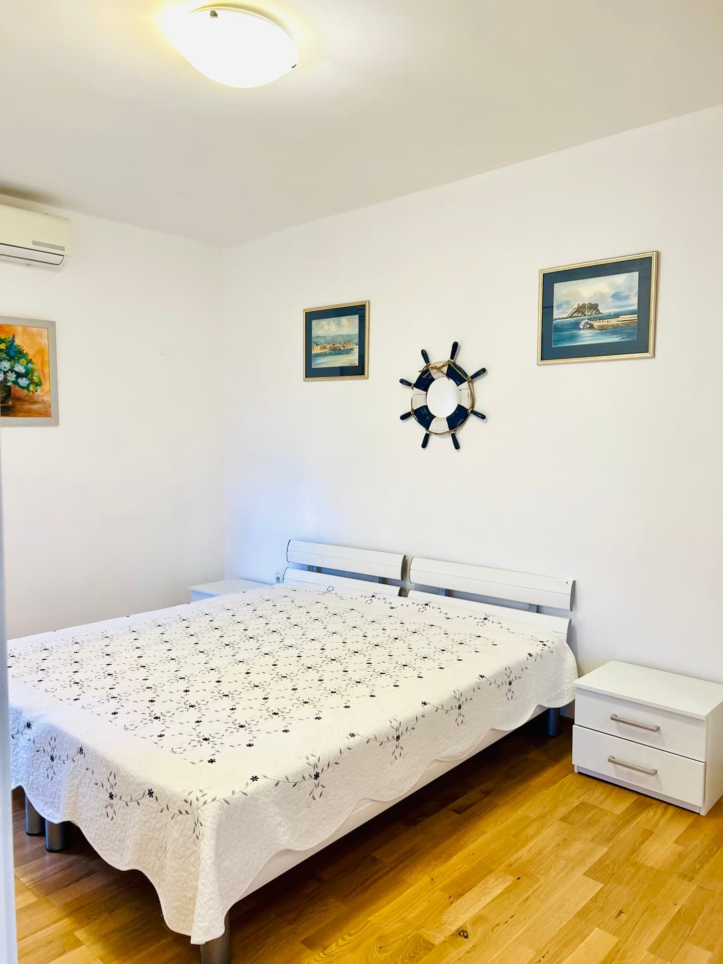 Bright bedroom with a double bed in an apartment in Petrovac, Montenegro: nautical decor and parquet flooring.