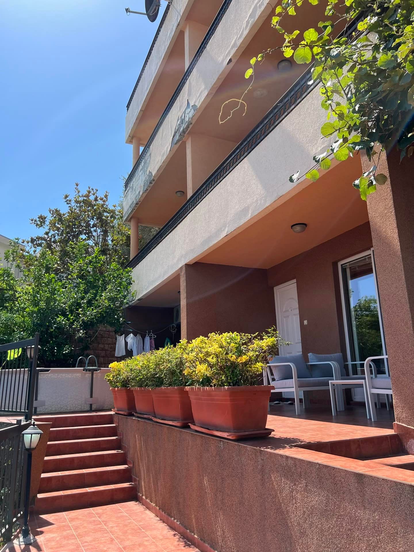 House facade with a terrace, garden furniture, and plants in Petrovac, Montenegro. View of the apartments from the street.