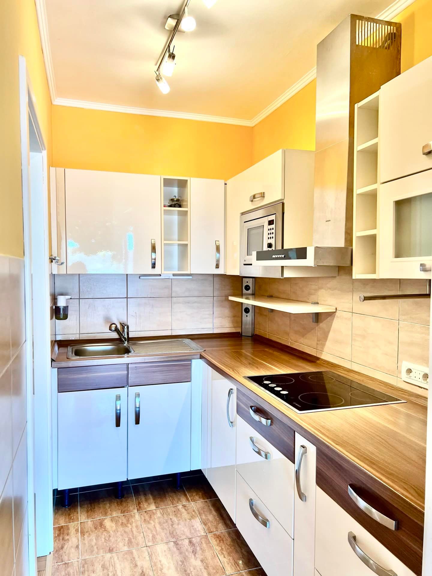 Modern kitchen in an apartment in Petrovac, Montenegro: white glossy cabinets, built-in appliances, and a tiled backsplash.
