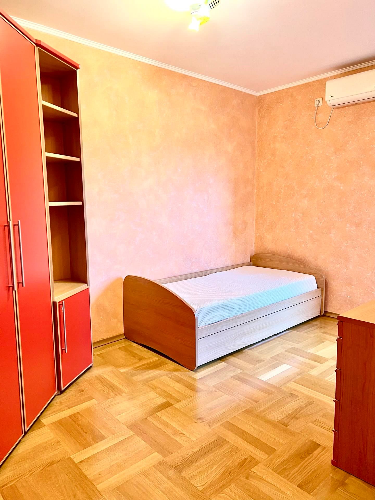 Bedroom in an apartment in Petrovac, Montenegro: single bed, red wardrobe, parquet flooring, and wall-mounted air conditioner.
