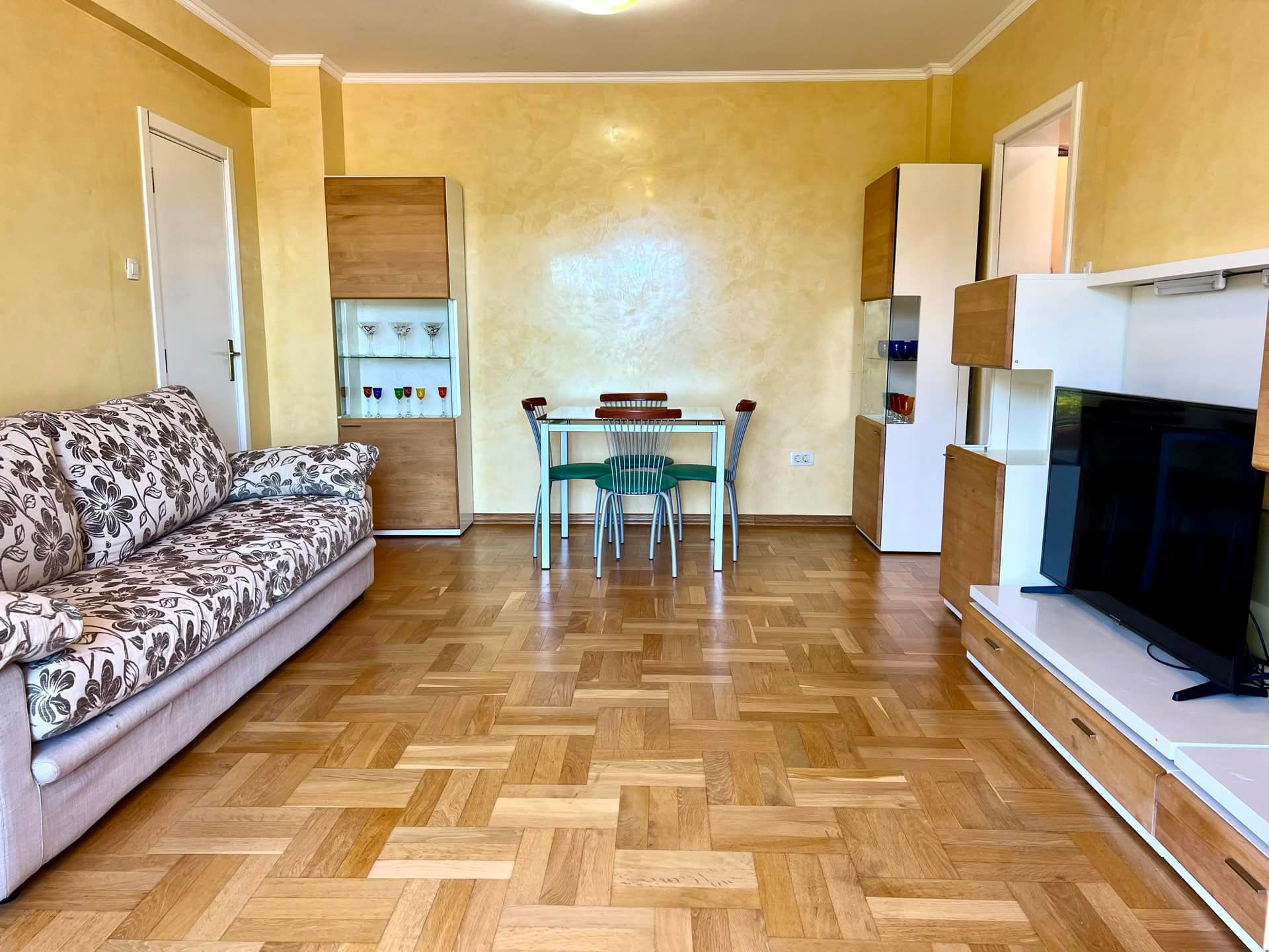Living room in an apartment in Petrovac, Montenegro: parquet flooring, a soft sofa, a dining area, and a modern TV wall unit.